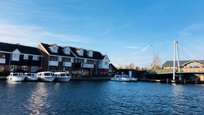 A waterfront property with multiple boats docked, a row of houses, and a bridge in the background. - Hotel Wroxham (Norwich)