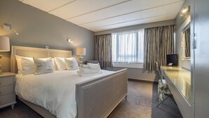 A hotel room with a large bed, a bedside table, a lamp, a mirror, and a window with curtains. - Hotel Wroxham (Norwich)