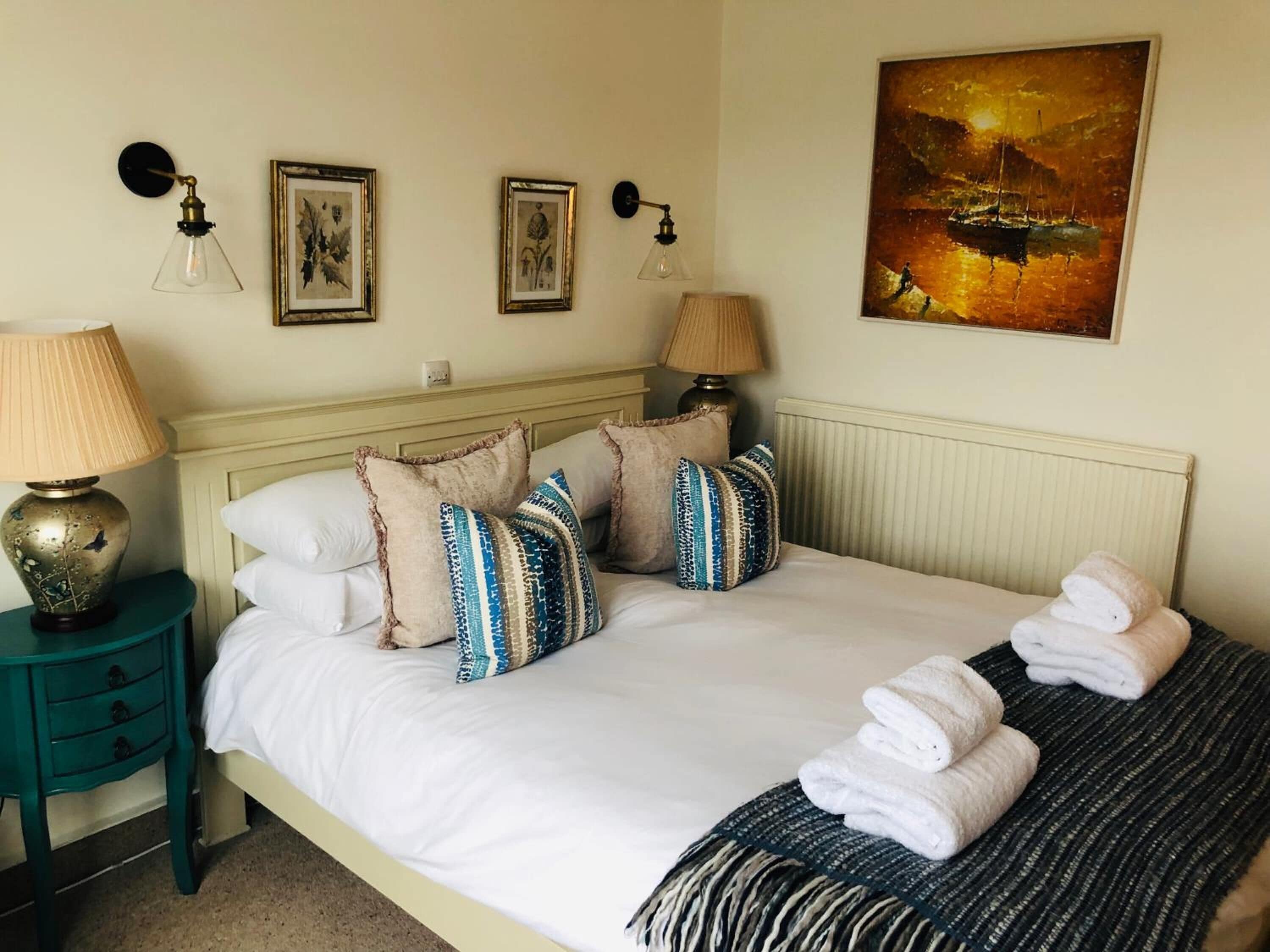 A neatly made bed with white linens, multiple pillows, and a folded towel on a striped blanket.
