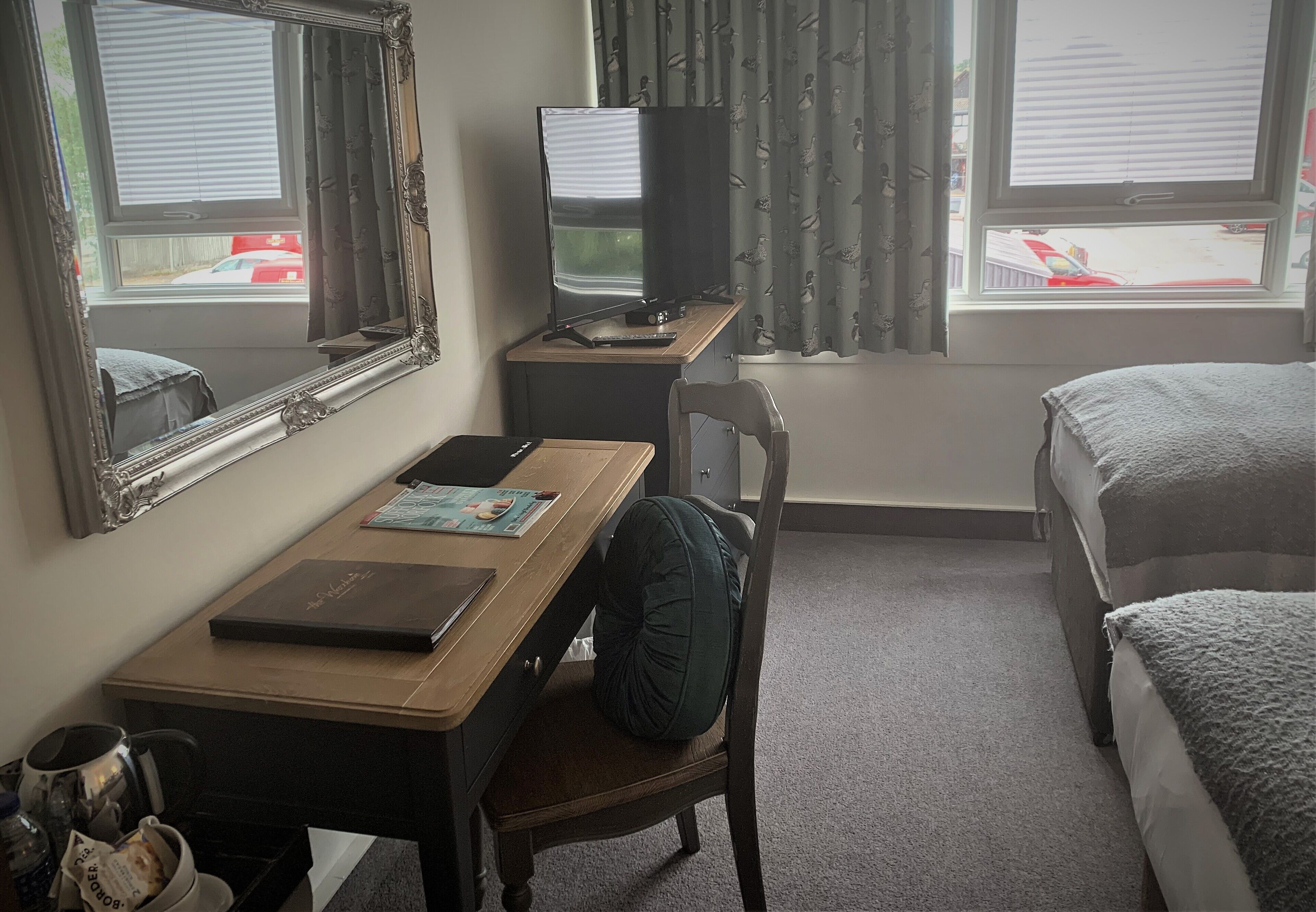 A hotel room with a desk, chair, television, and two beds.