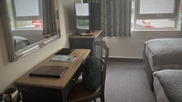 A hotel room with a desk, chair, television, and two beds.