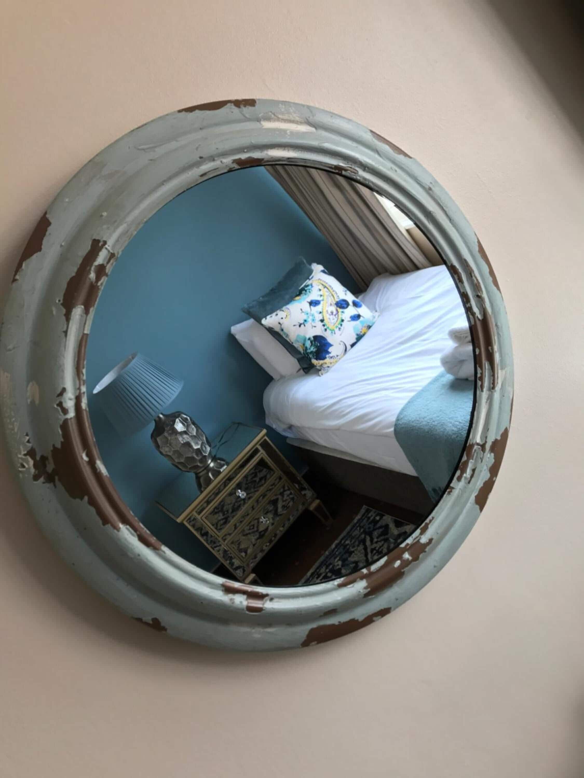 A bedroom with a bed, a nightstand, a dresser, and a mirror with peeling paint.