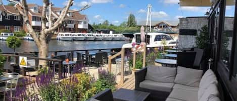 An outdoor seating area with wicker furniture, overlooking a marina with boats and houses in the background.