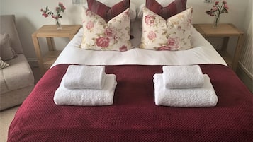 A neatly made bed with floral pillows, a red blanket, and two folded towels.