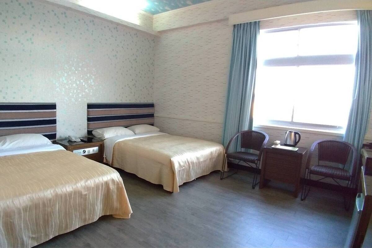 Une chambre d’hôtel avec deux lits, un bureau, une chaise et une fenêtre avec des rideaux.