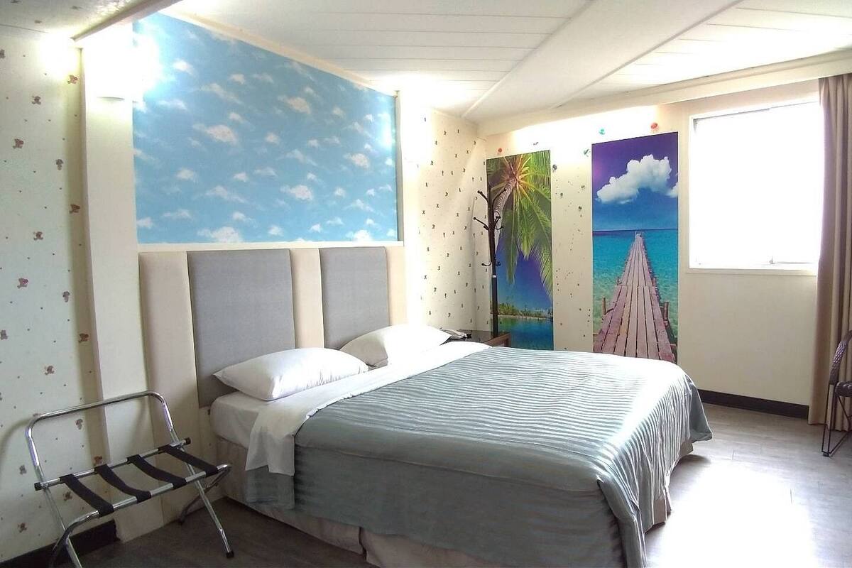 Une chambre d’hôtel avec un lit, une chaise, un bureau et une fenêtre avec des rideaux.