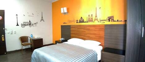 A hotel room with a bed, a chair, a nightstand, and a wall decorated with cityscape silhouettes.