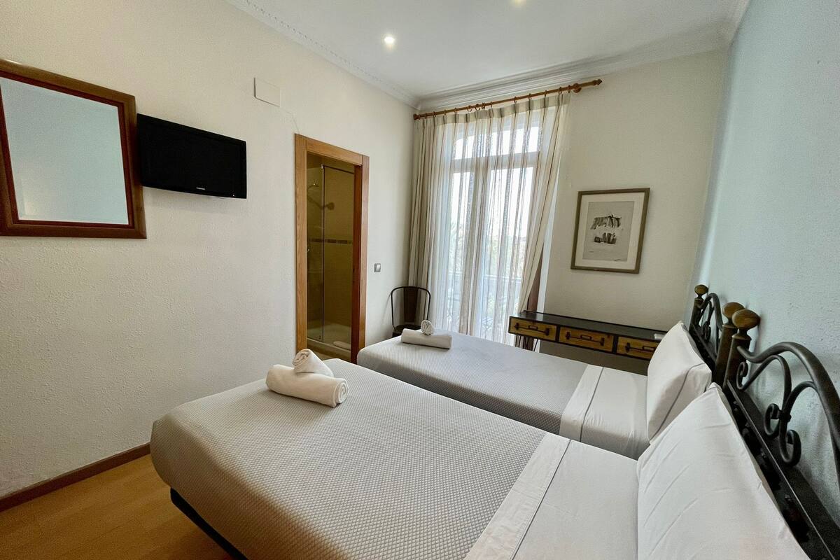 Habitación de hotel con dos camas, televisión, ducha y ventana con cortinas.
