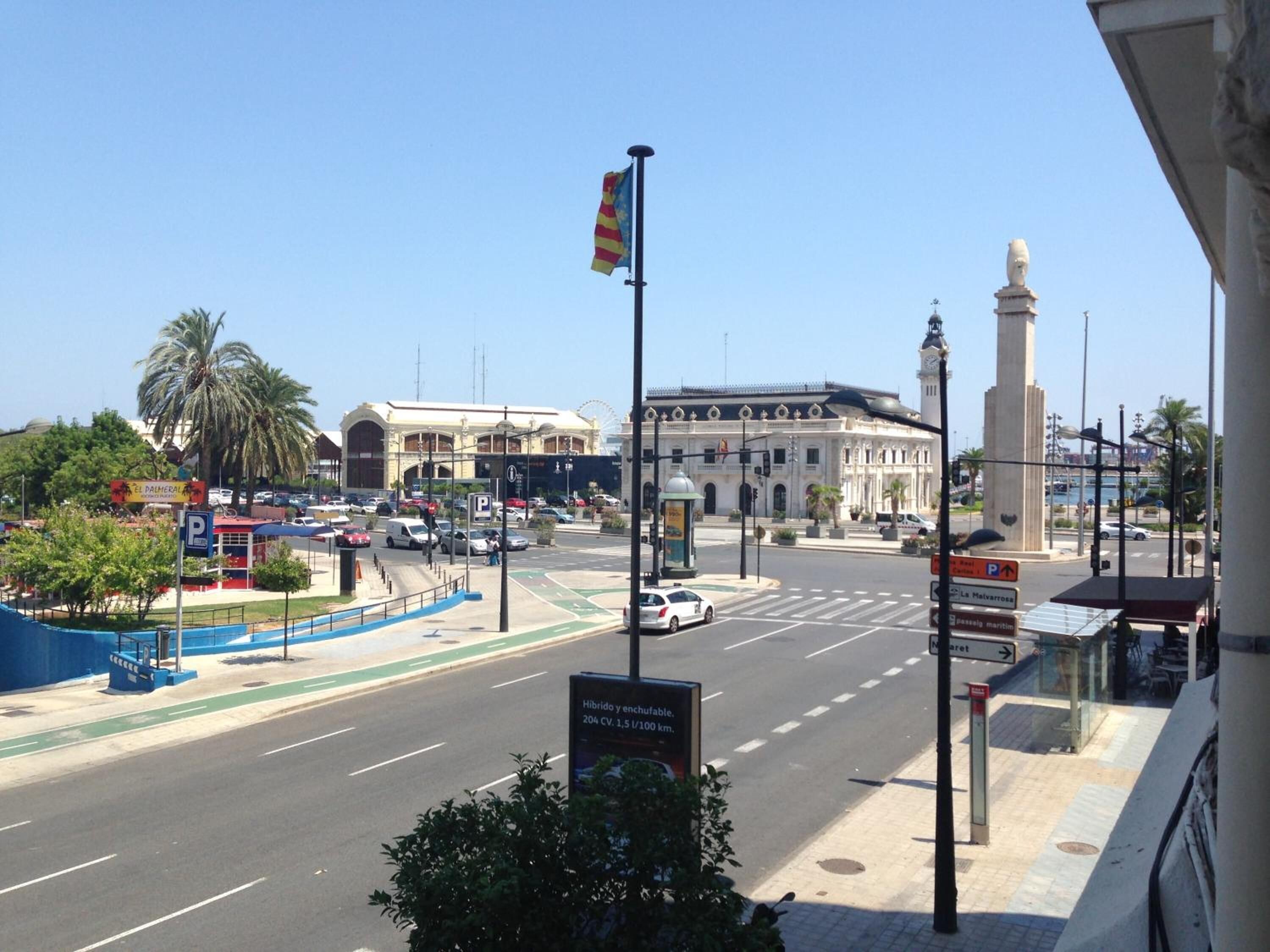 A city street with a prominent building, a flag, and a monument.
