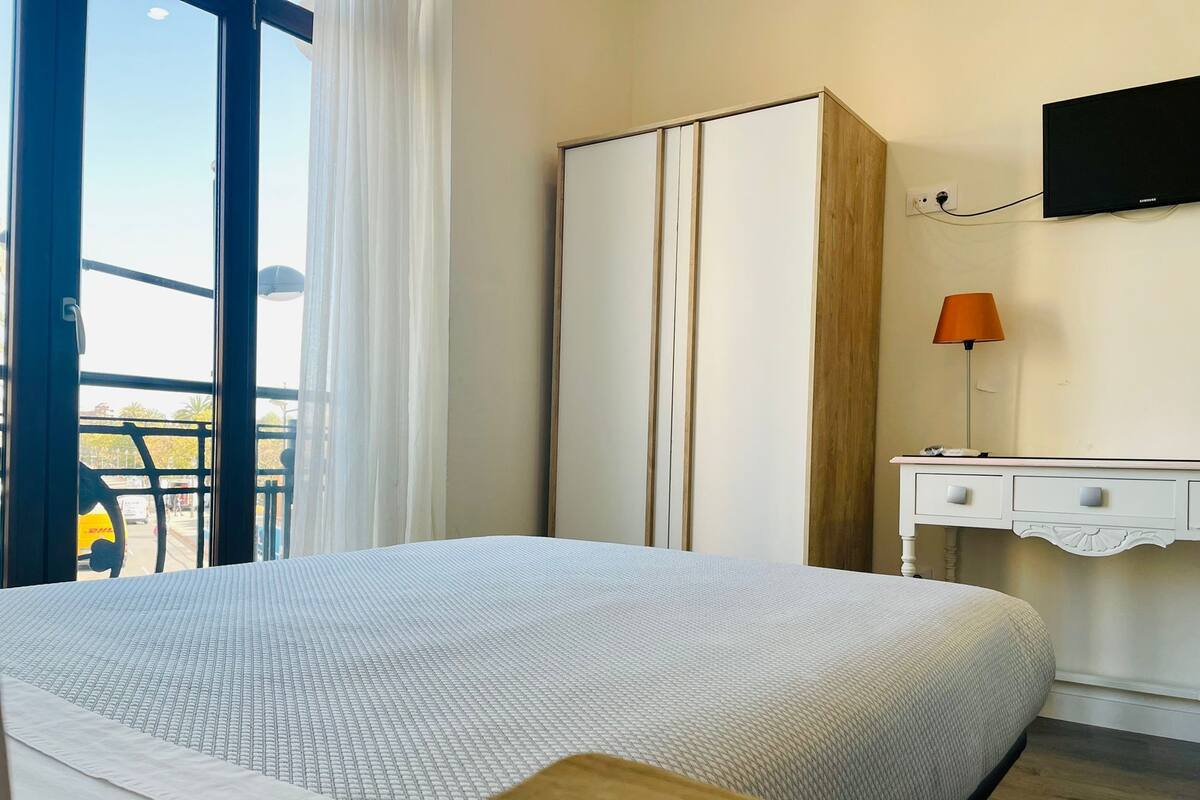 Una habitación de hotel con cama, armario, escritorio con lámpara y televisión en la pared.