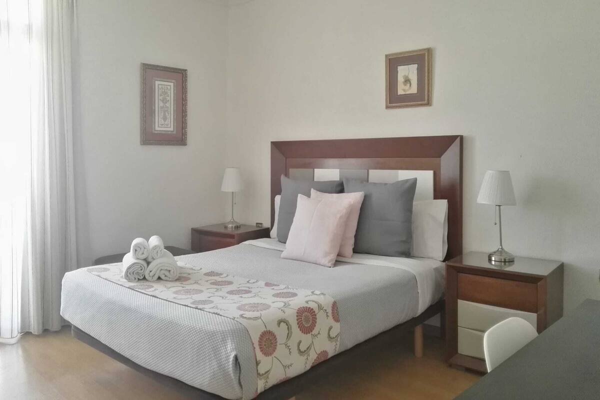 Una habitación de hotel ordenada con una cama grande, dos mesitas de noche, un escritorio y una silla.