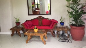 A living room with a red sofa, wooden coffee table, two side tables, a large mirror, and potted plants. - Kode Inn (Tagbilaran)