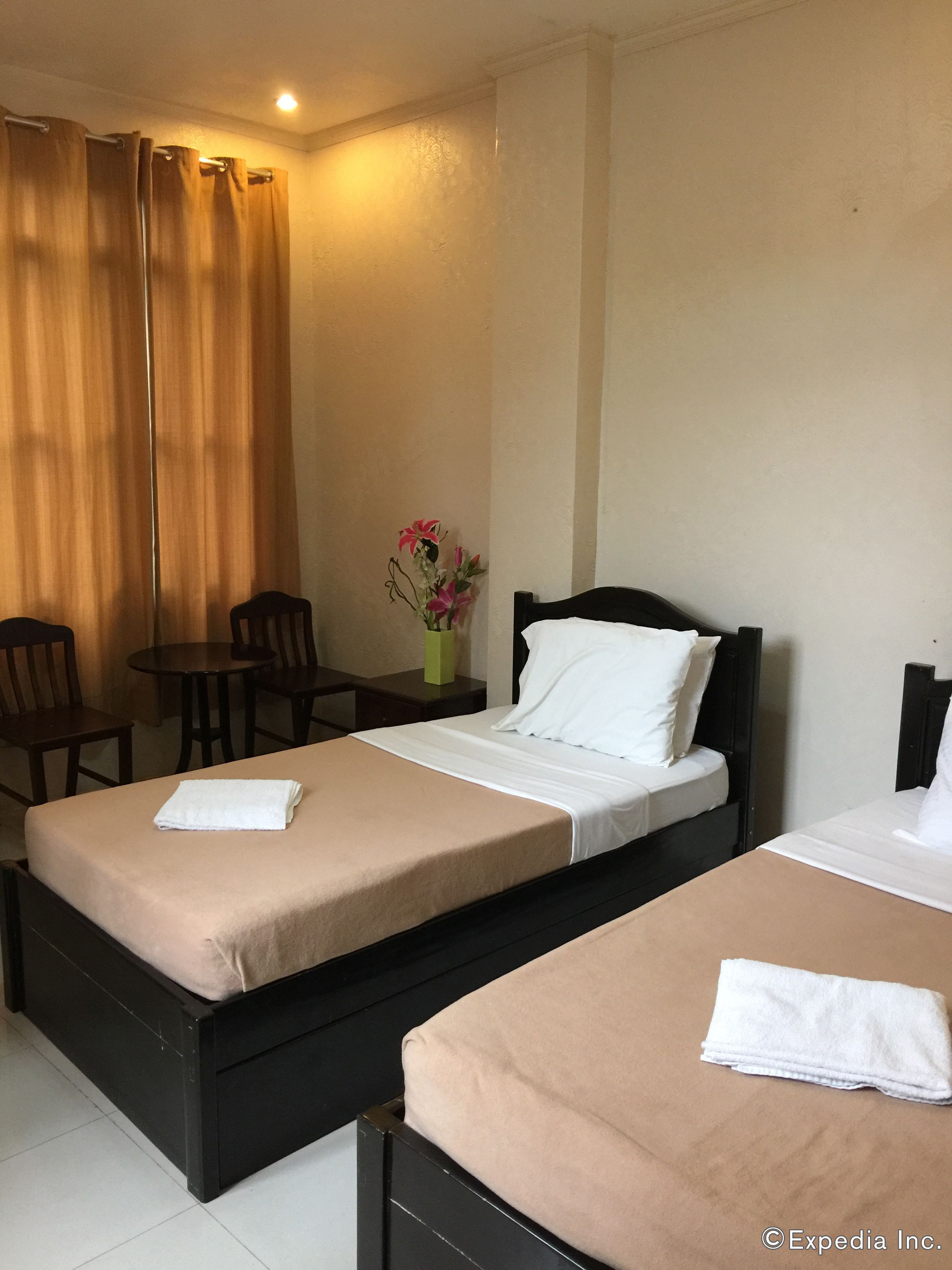 A hotel room with two beds, a small table, chairs, and a vase with flowers.