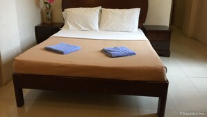 A neatly made bed with white pillows and a brown bedspread, flanked by two nightstands with a vase of flowers on one. - Kode Inn (Tagbilaran)