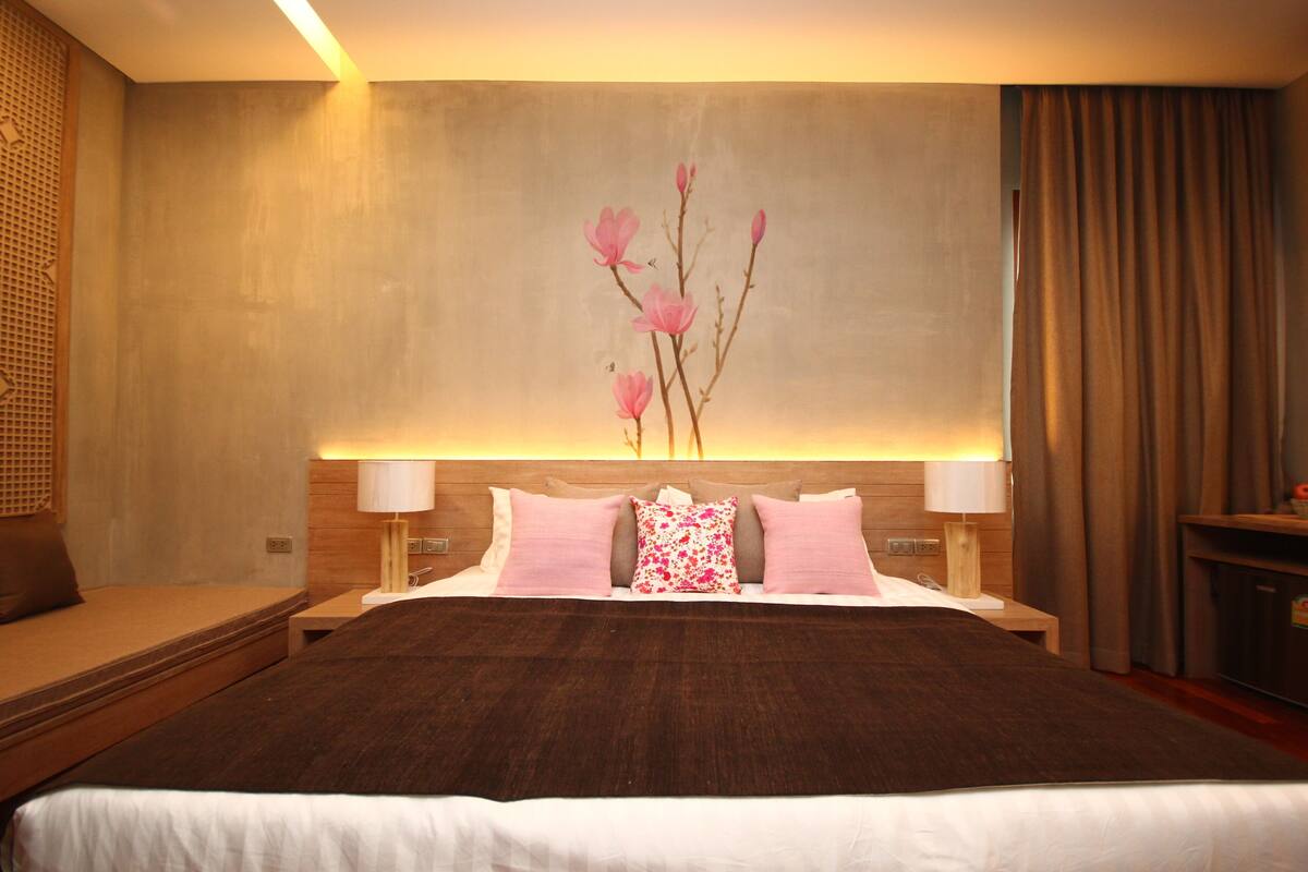 A hotel room with a large bed, two bedside tables with lamps, a wooden headboard, and a wall-mounted artwork of pink flowers.
