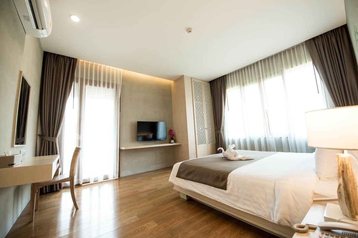A modern hotel room with a large bed, a desk with a chair, a television, and a bedside table with a lamp.