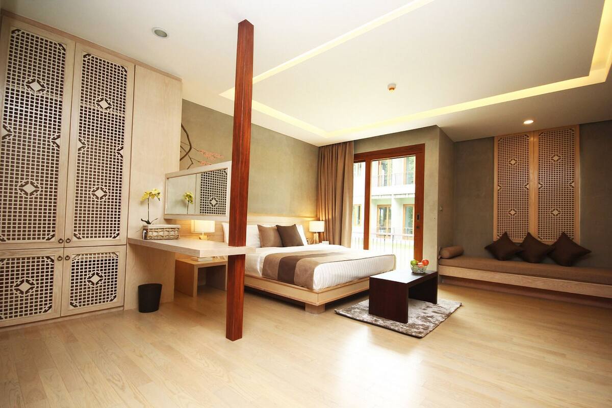 A modern hotel room with a large bed, a desk, a sofa, and a large window.