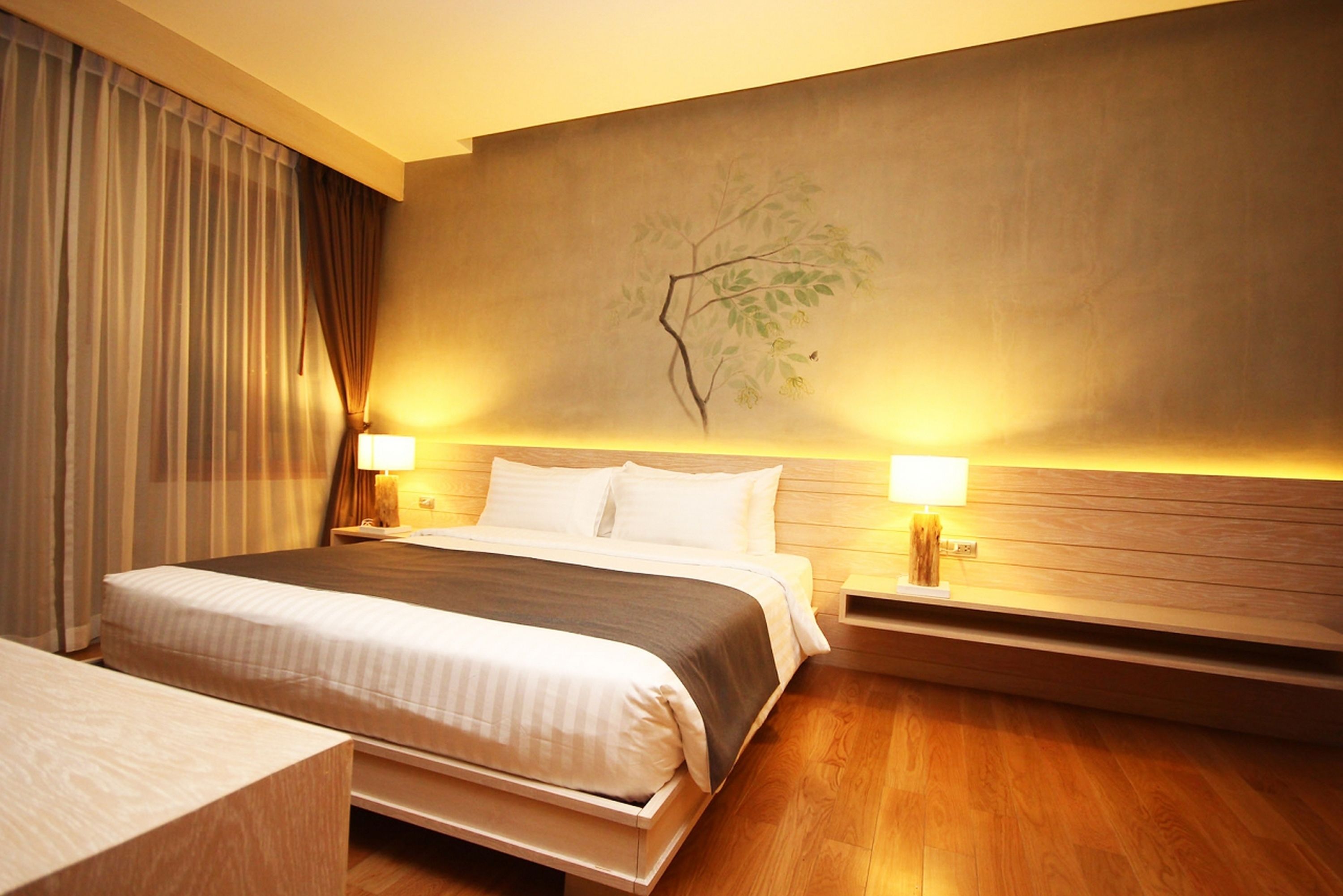 A hotel room with a large bed, two bedside tables with lamps, a wooden headboard, and a wall-mounted painting.
