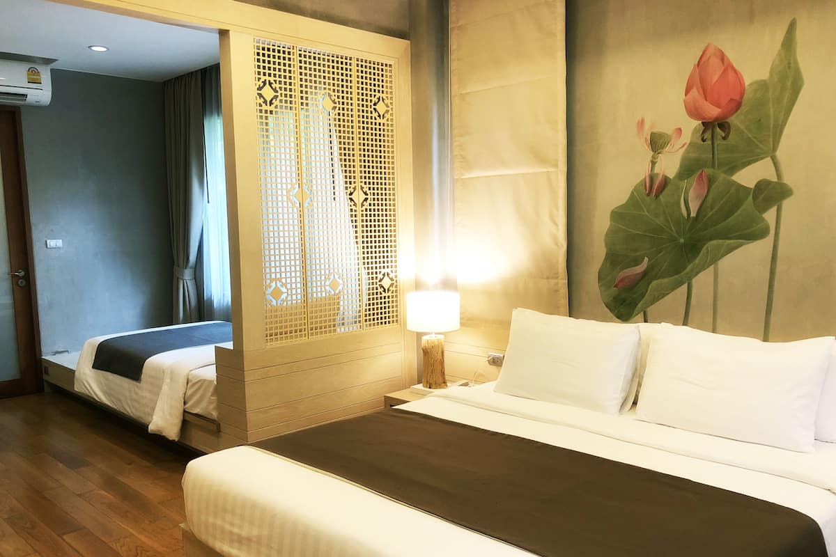 A hotel room with a large bed, a bedside table with a lamp, a decorative screen, and a wall painting of a lotus flower.
