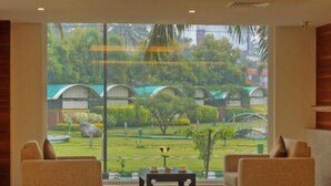 A spacious room with two sofas facing a large window, a small table, and a polished floor. - Hotel Le Ruchi the Prince (Mysore)