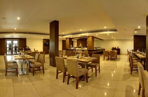 A spacious hotel dining area with multiple tables and chairs, a central bar area, and a modern interior design.
