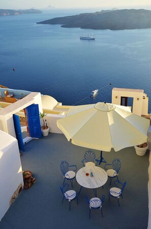 An outdoor seating area with a table and chairs, overlooking a body of water with boats. - Fira white residence (Santorini)