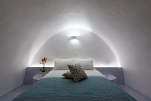 A cozy, arched bedroom with a bed centered under a skylight, flanked by two bedside tables and a potted plant. - Fira white residence (Santorini)