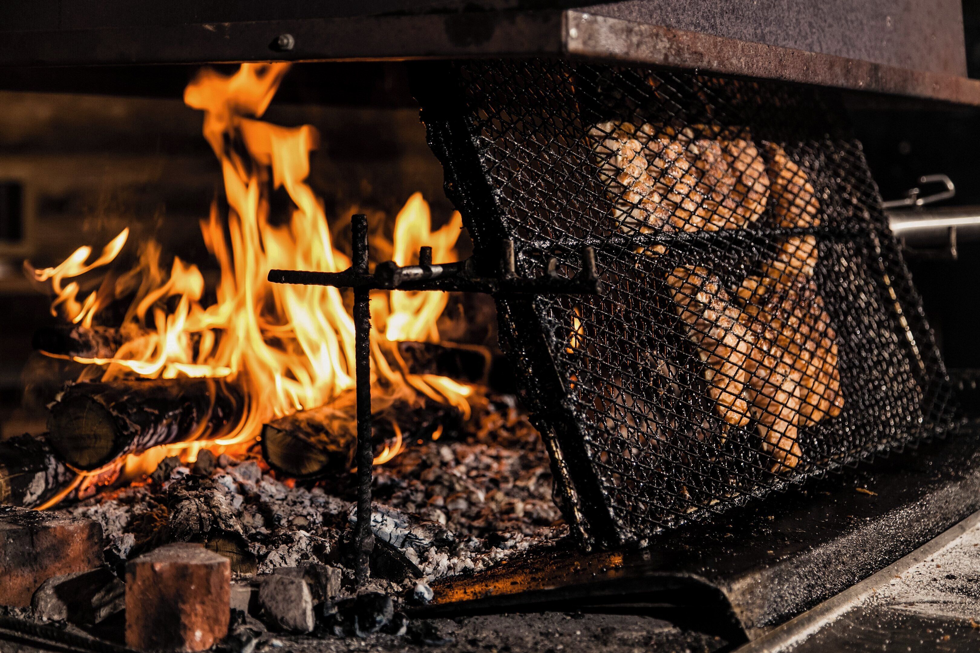 Un gril recouvert d’une grille métallique, placé au-dessus d’un feu, avec des flammes visibles et du bois en combustion.