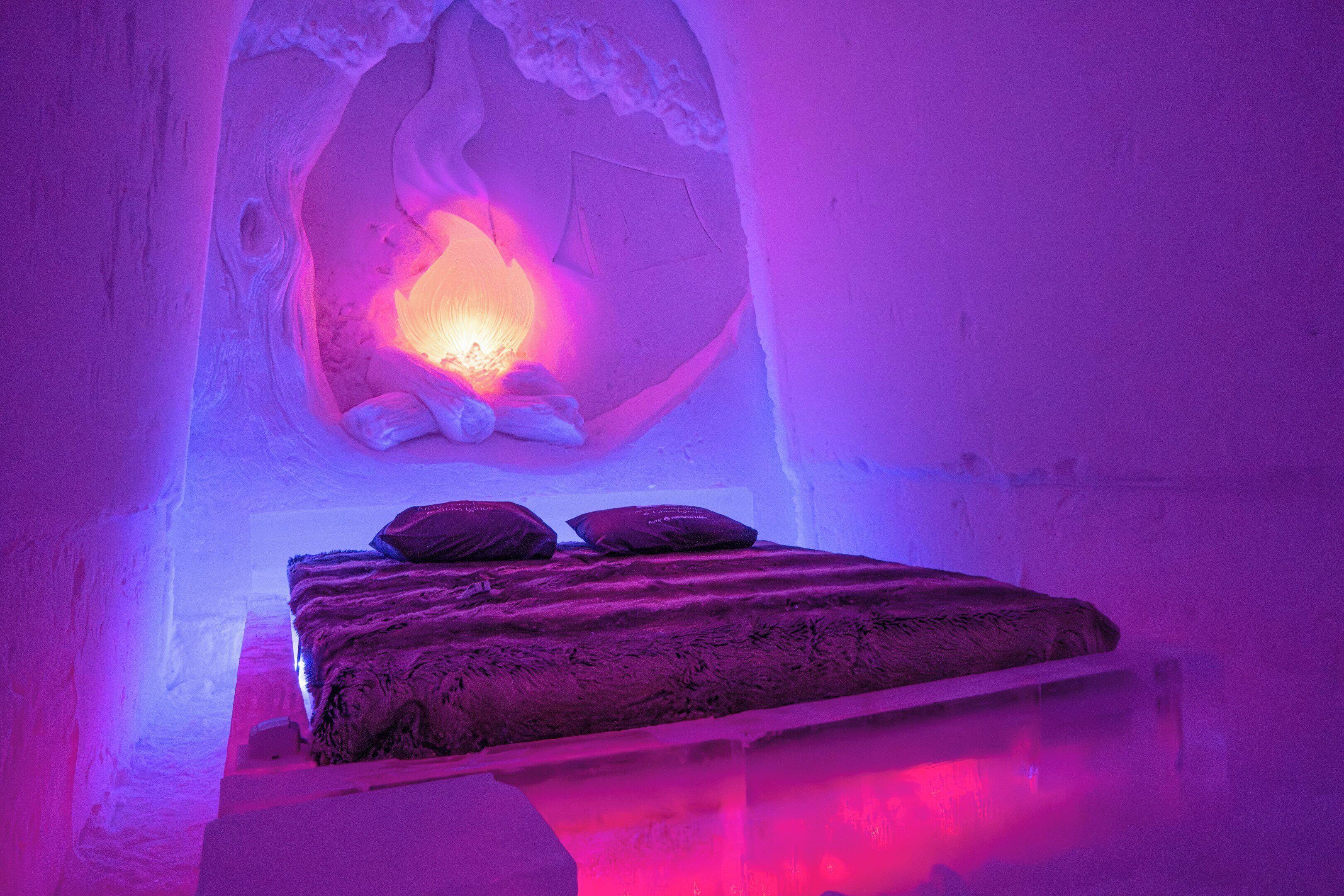 Una stanza di un hotel di ghiaccio con un letto, cuscini e una scultura di ghiaccio al centro.