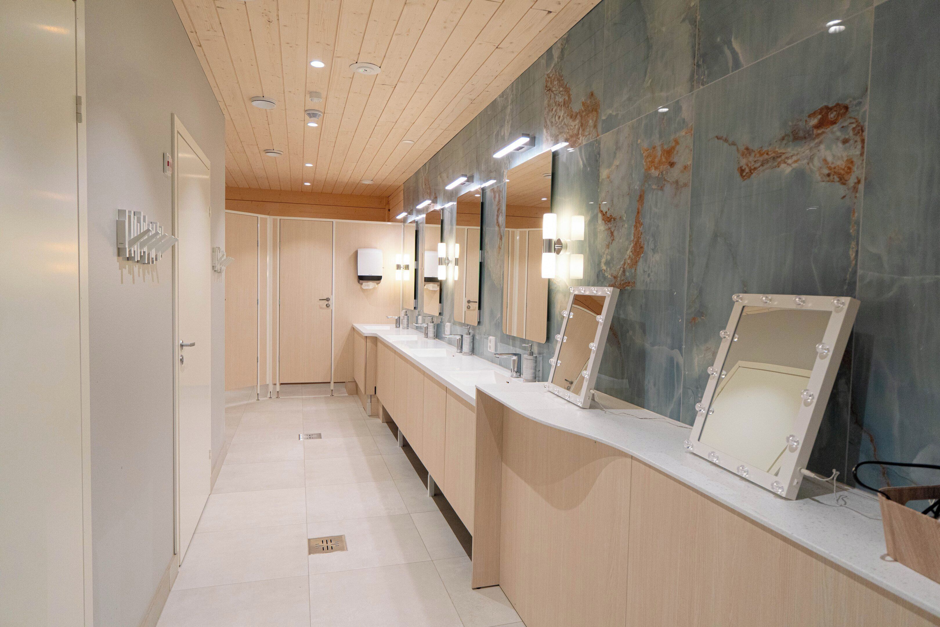 Un baño moderno con un tocador amplio, varios espejos y una pared de mármol.