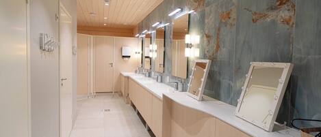 Un baño moderno con un tocador amplio, varios espejos y una pared de mármol.