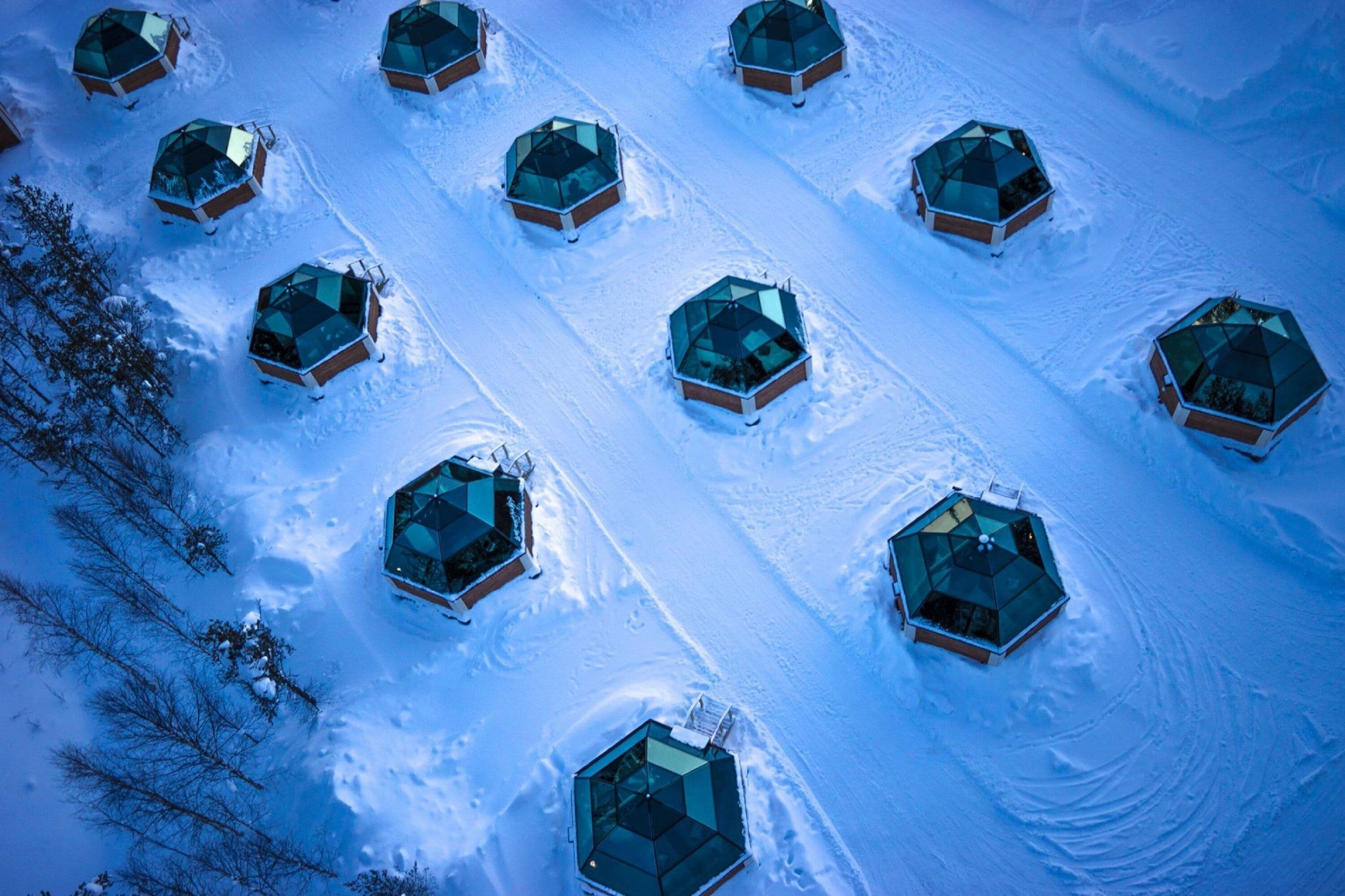 A series of hexagonal glass-roofed cabins arranged in a grid pattern on a snow-covered slope.