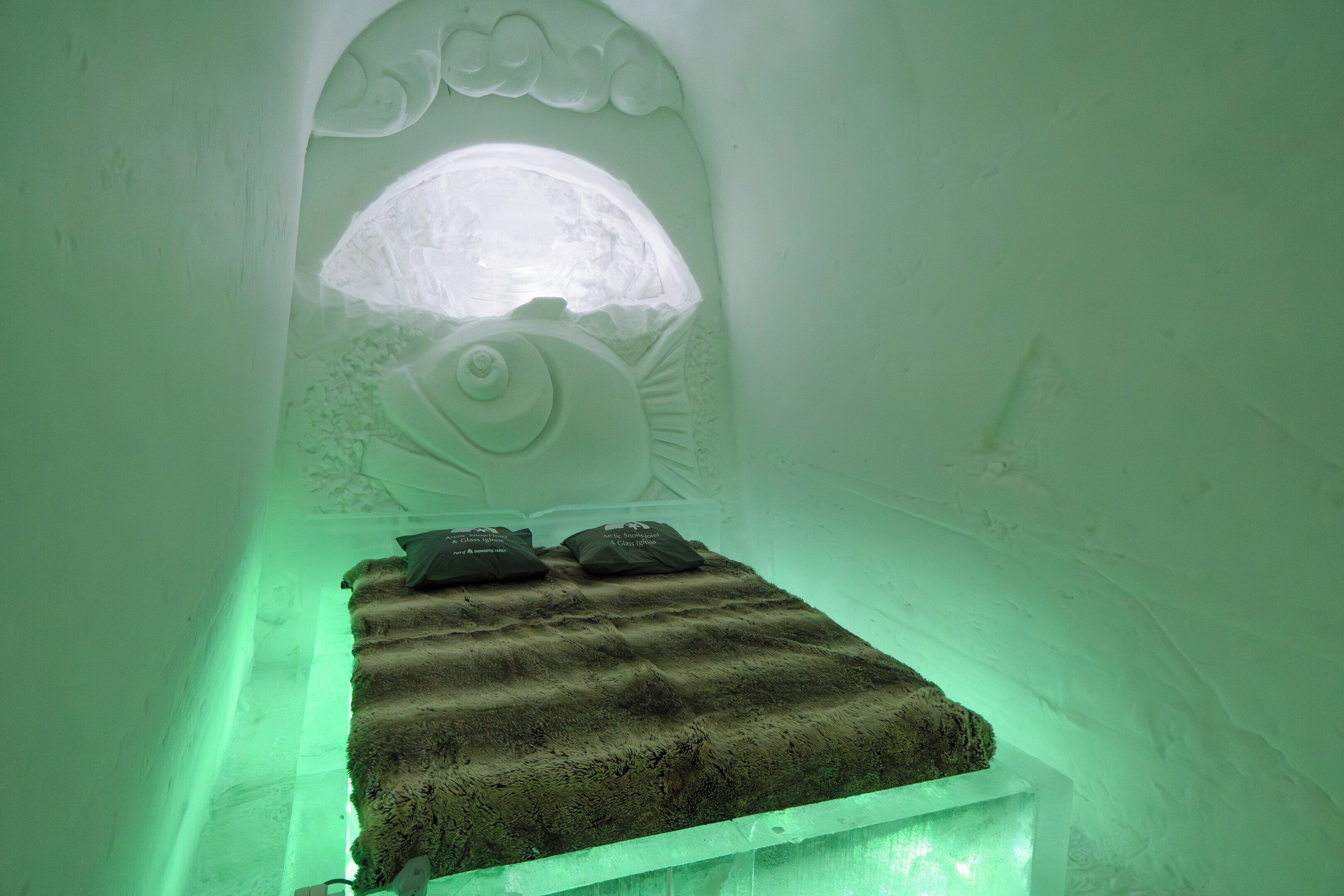 An ice hotel room with a bed, pillows, and a carved wall design.