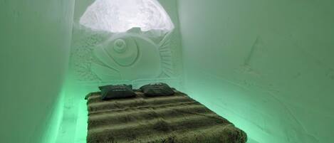 An ice hotel room with a bed, pillows, and a carved wall design.