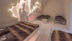 An ice hotel room with a bed, a wooden bench, and a unique ice sculpture. - Arctic SnowHotel & Glass Igloos (Rovaniemi)