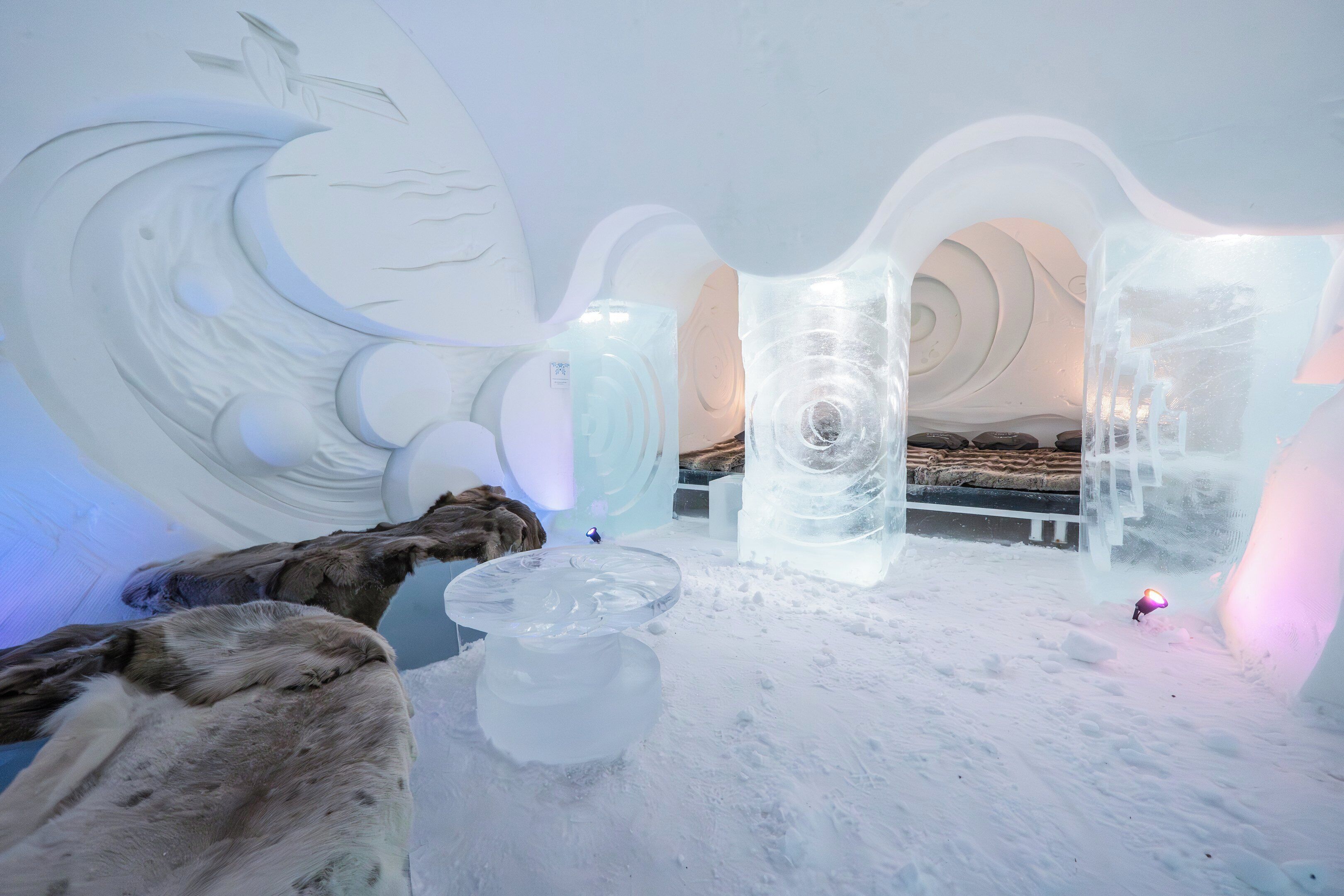 Una habitación de hotel de hielo con cama, esculturas de hielo y suelo cubierto de nieve.