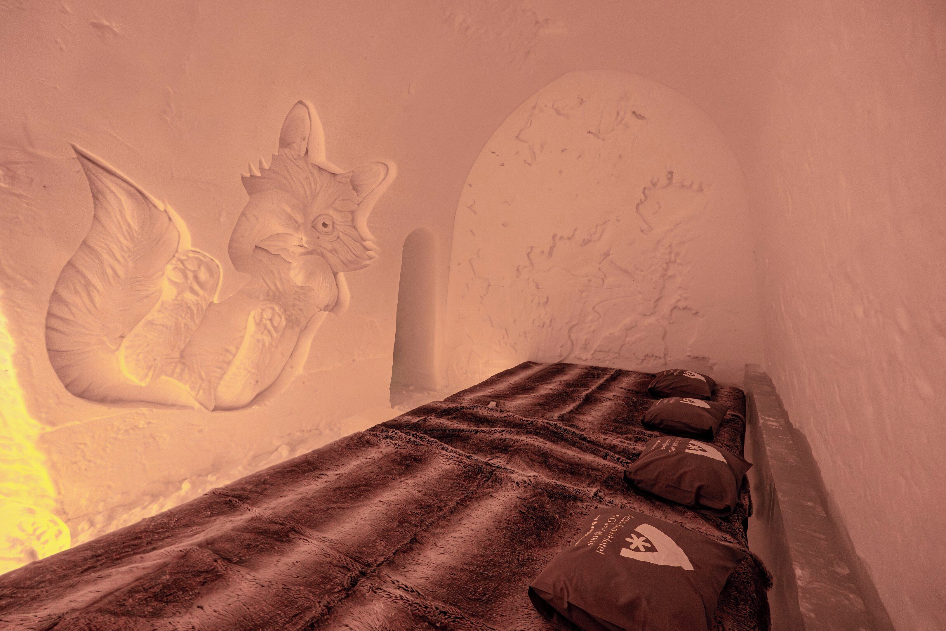 Une pièce comprenant un lit, des oreillers et un mur orné d’une sculpture représentant un chat et un ange.