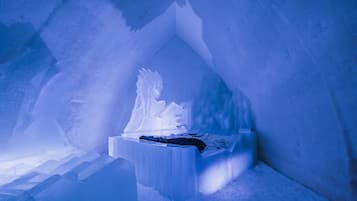 Interior de un hotel de hielo con una escultura central de hielo y un banco.