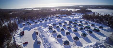 An aerial view of a snow-covered area with multiple dome-shaped cabins arranged in rows, a snowmobile parked, and a clear sky.