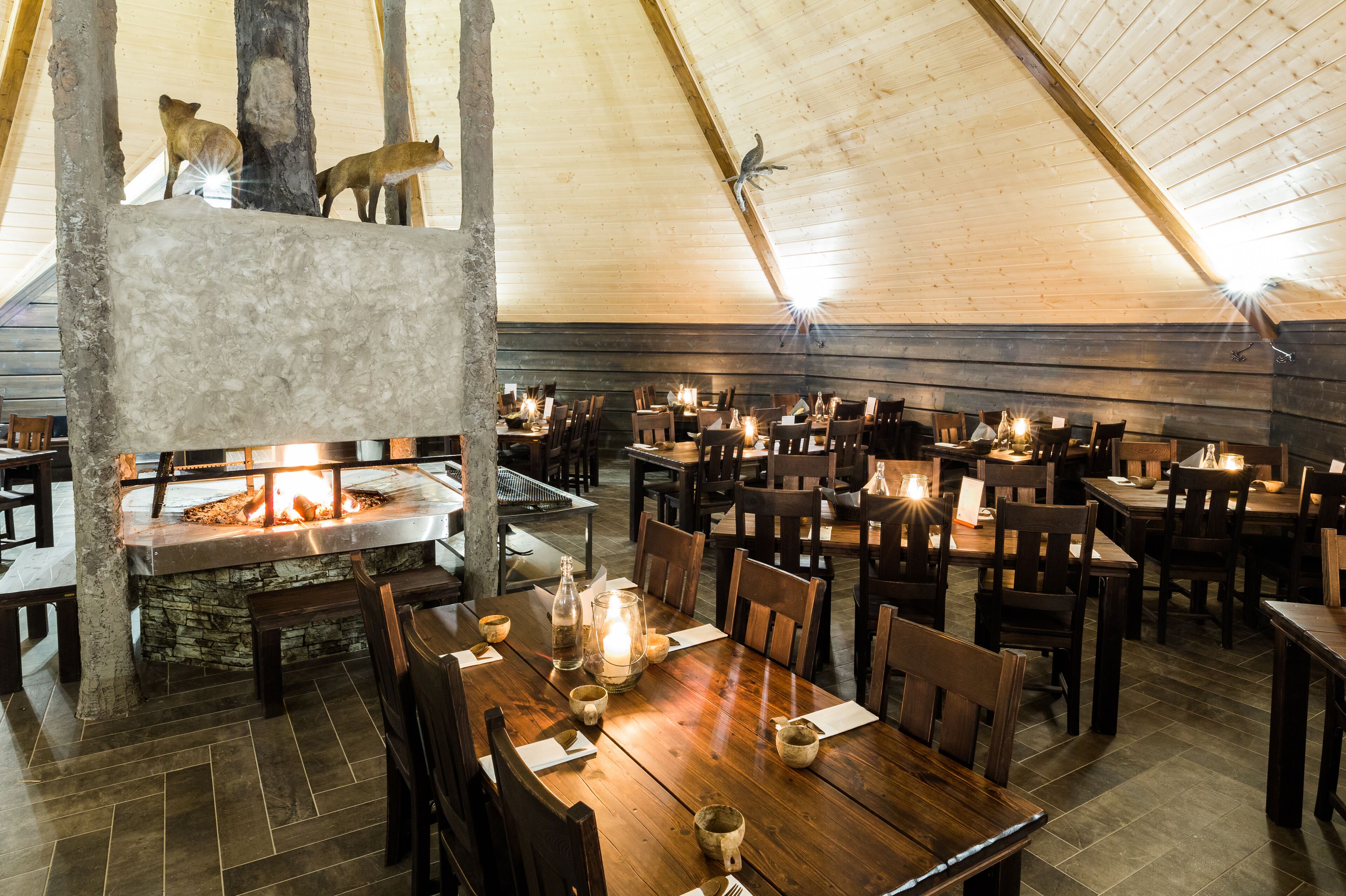 Un restaurante con mesas y sillas de madera, una chimenea de piedra y un techo alto.