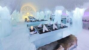 An ice bar with tables set for dining, featuring ice sculptures and candles. - Arctic SnowHotel & Glass Igloos (Rovaniemi)