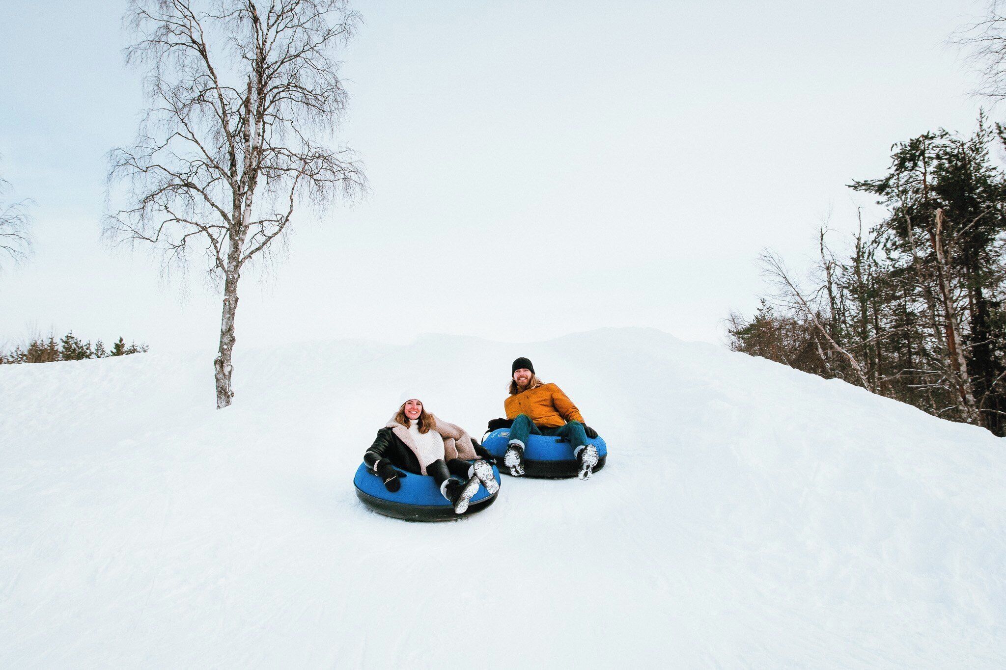 Two people in snow tubes on a snowy slope with trees in the background.