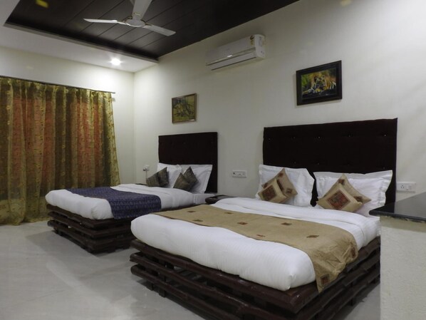 Habitación de hotel con dos camas, cada una con cabecero oscuro, ropa de cama blanca y almohadas decorativas. Incluye un ventilador de techo, aire acondicionado y un cuadro en la pared.