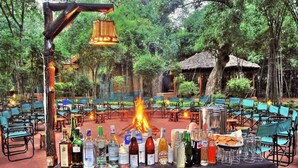 Een terras met een vuurkorf, tafels, stoelen en verschillende flessen en glazen.