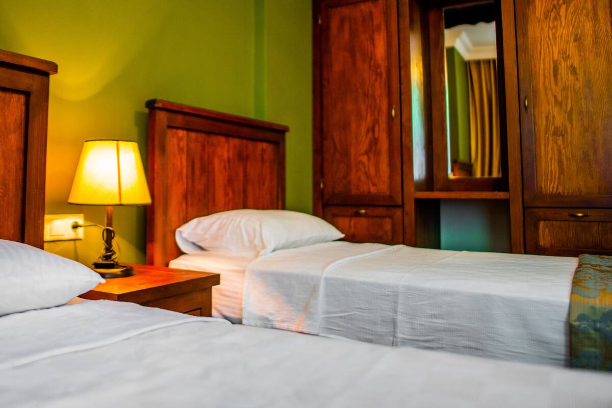 A hotel room with two single beds, a wooden nightstand with a lamp, and wooden wardrobes.