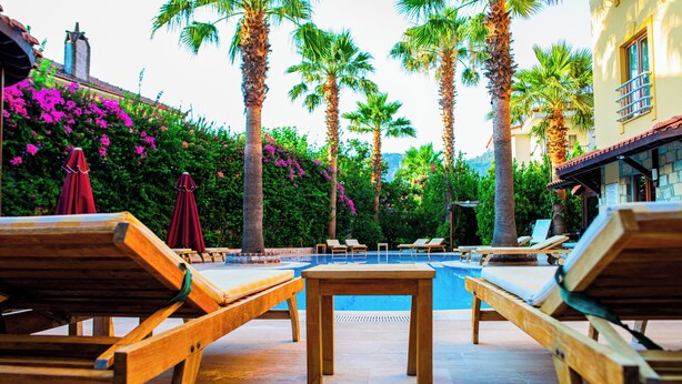 A poolside area with lounge chairs, a table, and palm trees. - Dores Residence (Marmaris)