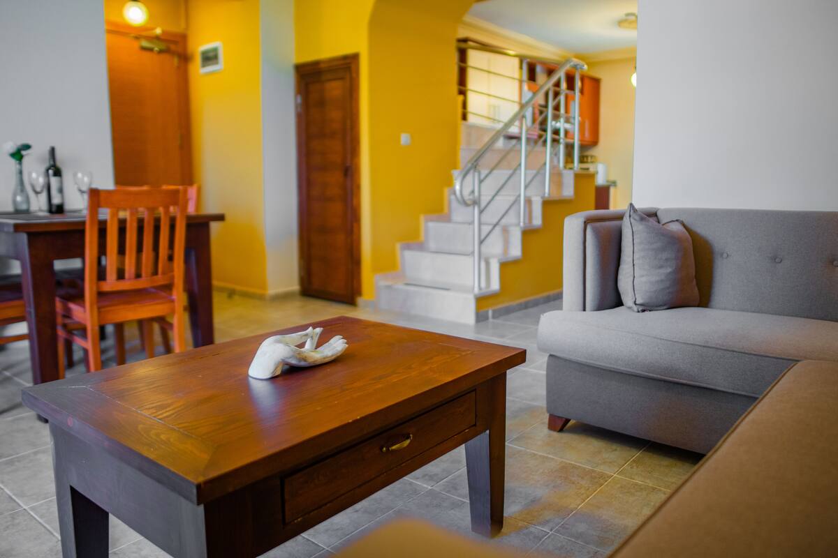 A living room with a wooden coffee table, a grey sofa, and a staircase in the background.