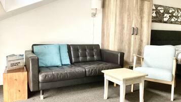 A living room with a black leather sofa, a light blue armchair, a wooden cabinet, and a small wooden table.
