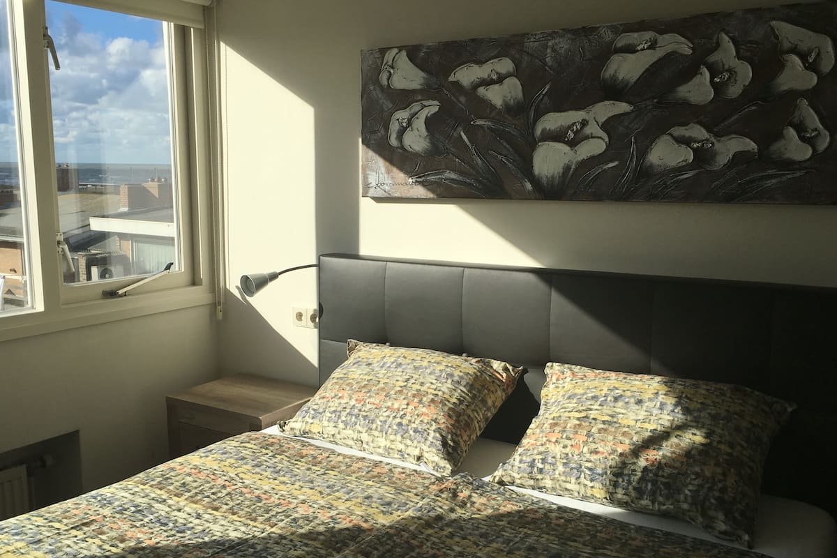 Quarto com cama, janela e um quadro na parede.