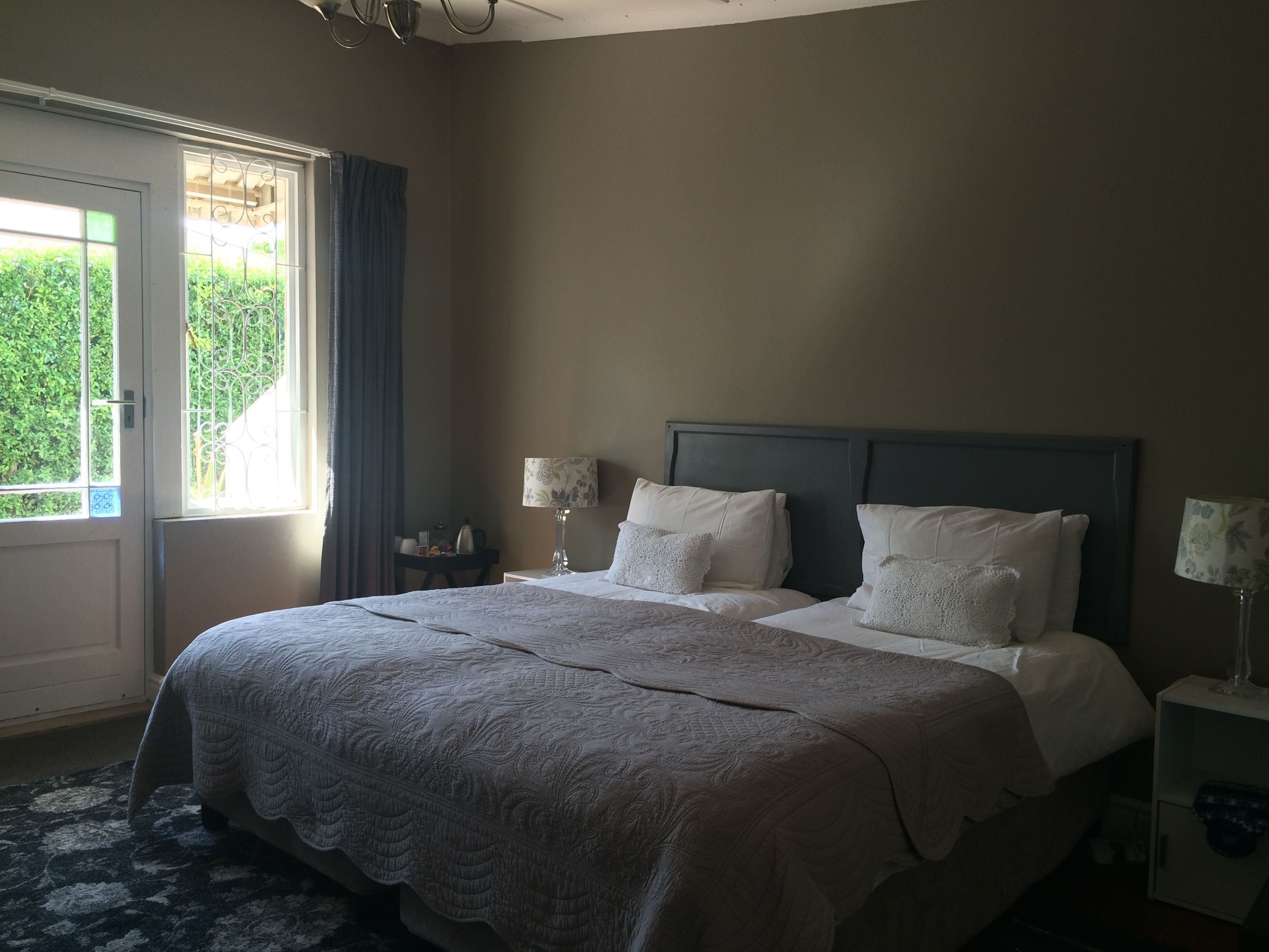 A hotel room with a large bed, two bedside tables with lamps, a window with curtains, and a view of greenery outside.